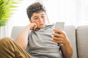 teen boy with curly hair on phone learning about the signs of bullying