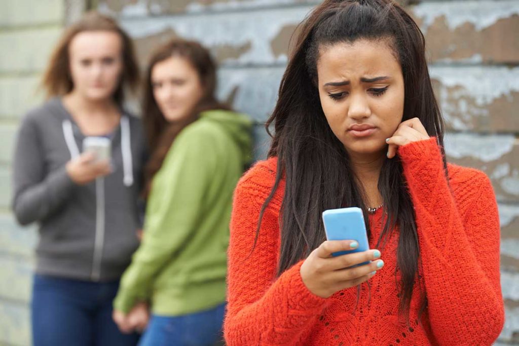 girl on phone with others in background learning about cyberbullying